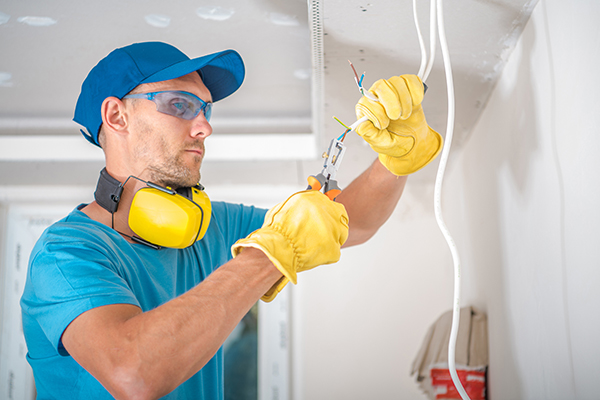 Electrician in Protective Gloves and Glasses Doing Illumination Installation Work Stripping Cables with Professional Wire Stripper.