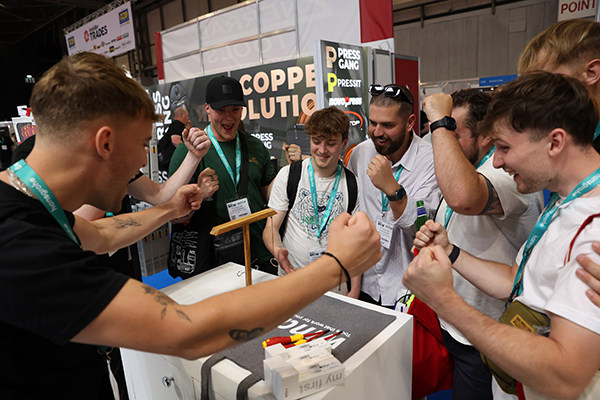 8 people stood around a gadget celebrating, at the InstallerSHOW event.