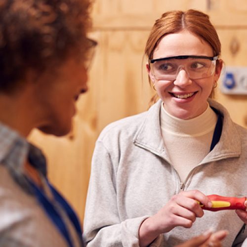 2 people, one holding a tool, and wearing Goggles, representing Schneider Electric apprenticeship programme